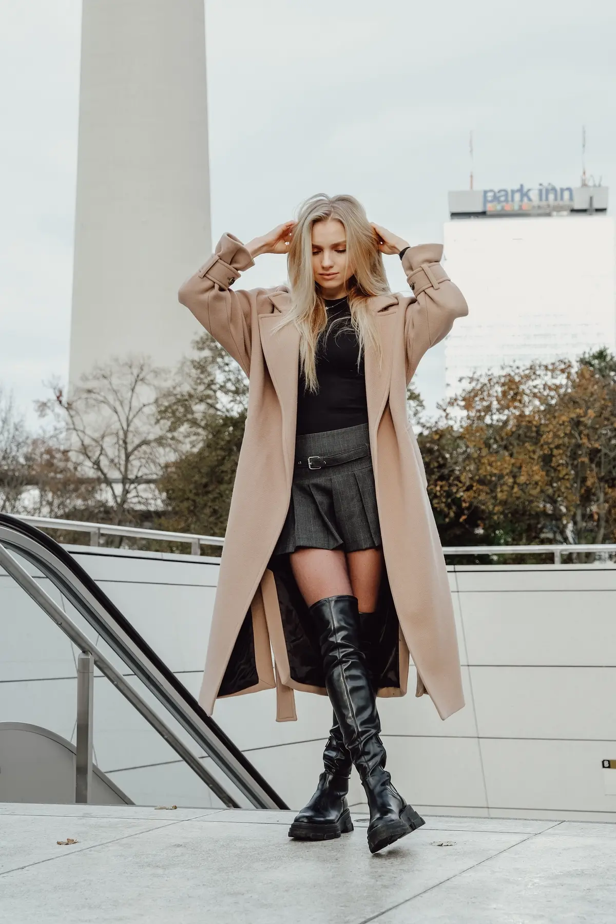 short pleated skirt paired with black top long brown coat and otk boots